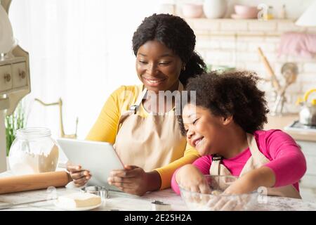 Mamma nera e bambina che controllano online la ricetta dell'impasto tablet digitale Foto Stock