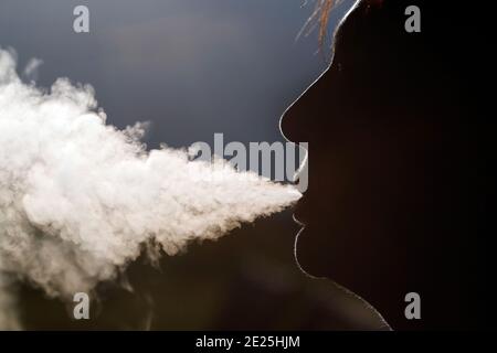 Profilo silhouette di una donna che fuma. Fumo bianco intenso. Francia. Foto Stock