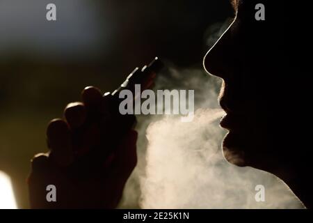 Profilo silhouette di una donna che fuma. Fumo bianco intenso. Sigaretta elettronica. Francia. Foto Stock