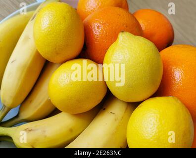 Una composizione colorata di frutta fresca disposta su un tavolo di legno. Gli ingredienti sono: Banane, arance e limoni Foto Stock