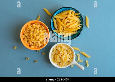 penne, farfalle tonde butterfly e ditalini tipo di pasta su fondo azzurro. pasta in ceramica. ciotola blu arancio bianco. astratto, pasta. t Foto Stock