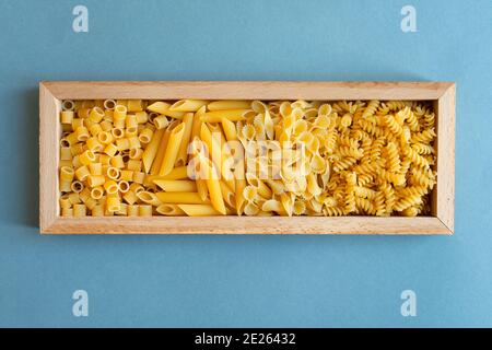 penne, farfalle tonde butterfly, trivella e ditalini tipo di pasta su fondo azzurro. pasta in una scatola di legno piatto. astratto, pasta. vista dall'alto pho Foto Stock