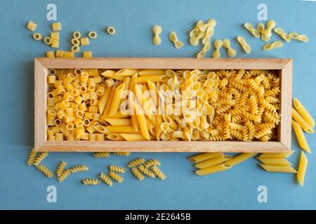 penne, farfalle tonde butterfly, trivella e ditalini tipo di pasta su fondo azzurro. pasta in una scatola di legno piatto. astratto, pasta. vista dall'alto pho Foto Stock