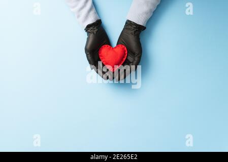 Concetto di giorno di San Valentino con un cuore rosso nelle mani Di una donna protetta da guanti medici durante il Covid-19 pandemia dell'infezione da coronavirus Foto Stock