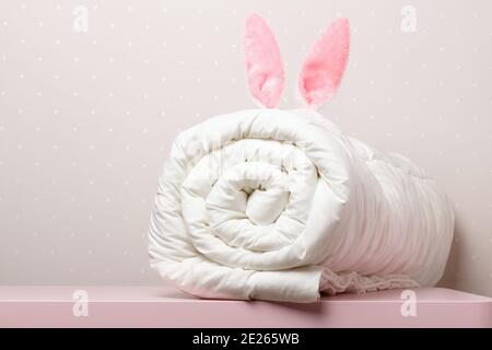 Sul tavolo si trova un caldo piumino ripiegato con orecchie di Pasqua coniglietto. Coperta per il letto. Spazio di copia. Foto Stock