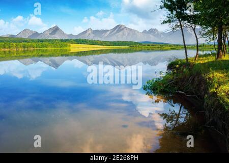 paesaggio composito di lago di montagna in estate. splendido paesaggio naturale in una mattina soleggiata. cielo e cresta che si riflettono nella calma superficie d'acqua. alberi Foto Stock
