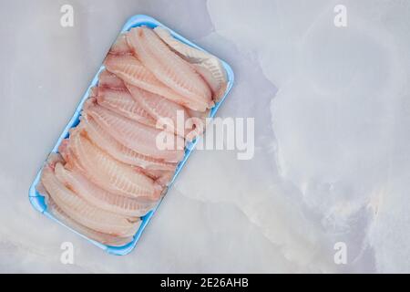 Filetto di tilapia in contenitore di plastica primo piano su fondo di marmo, spazio di copia, piatto Foto Stock