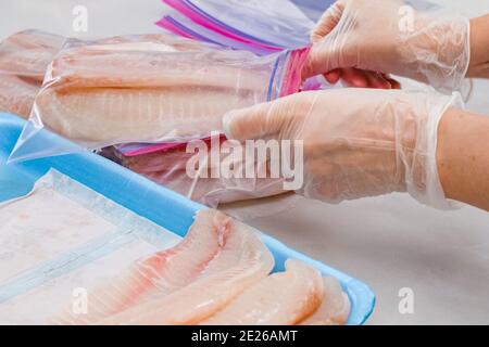 Filetto di pesce fresco crudo in sacchetti con chiusura a zip. Filetto di tilapia su sfondo di marmo chiaro, primo piano Foto Stock