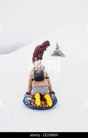 Un uomo rotola una donna su un tubo per un corda attraverso la neve in montagna - un forte blizzard sulle piste da sci - sfocatura dell'azione Foto Stock