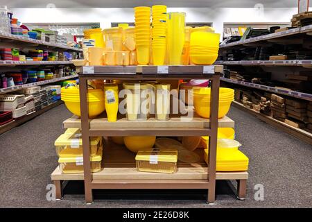 Le pentole gialle di plastica sono vendute al negozio. File di diversi utensili da cucina per la casa su scaffali in un supermercato. Foto Stock