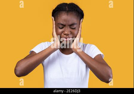 African American Donna che copre le orecchie che soffrono di otite, sfondo giallo Foto Stock