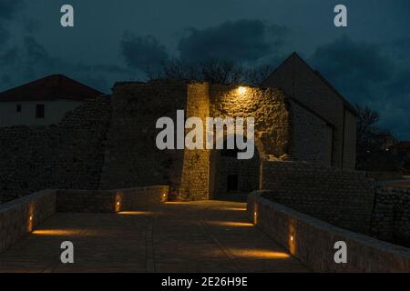 Antico cancello in pietra e ponte nella città medievale storica di Nin di notte. Dalmazia, Croazia. Foto Stock