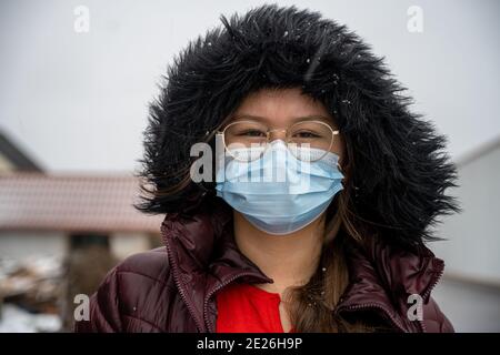 Una ragazza adolescente con in una giacca invernale con un cappuccio che indossa una maschera protettiva per il viso. Immagine a freddo e in condizioni di neve Foto Stock