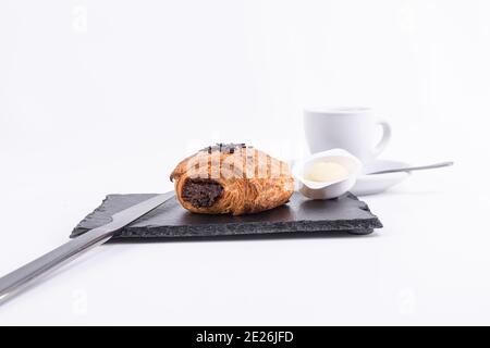 Primo piano di un croissant al cioccolato fresco con una tazza di caffè isolato su sfondo bianco Foto Stock
