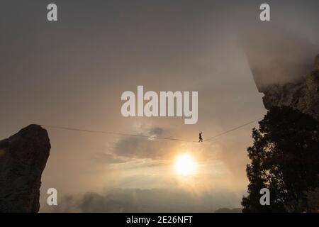 una persona che cammina un highline su un tramonto nuvoloso tra rocce grandi Foto Stock