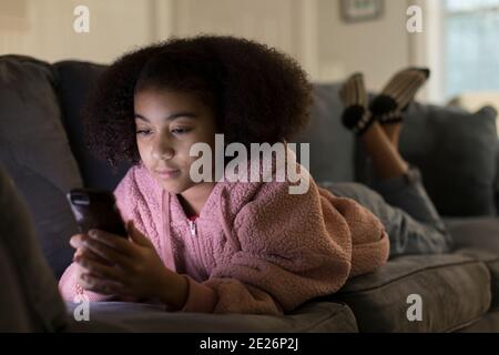 Ragazza bi-razziale di dieci anni che guarda il suo telefono cellulare mentre l Foto Stock