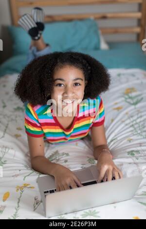 Dieci anni bisrazziale ragazza che lavora sul suo laptop Apple e. sorridente Foto Stock