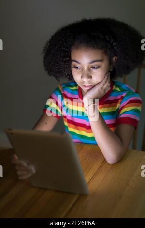 ragazza birazziale di dieci anni che guarda l'ipad al tavolo Foto Stock