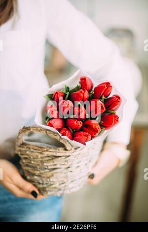 donna fiorista che tiene un cestino con tulipani rossi in carta bianca. concetto di consegna del negozio di fiori Foto Stock