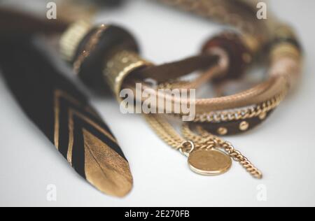 Accessori eleganti perle fatte a mano in metallo e pelle d'oro e eleganti piume nere con bordatura d'oro su sfondo bianco. Stile boho Foto Stock