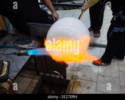 L'artista del vetro forma il vetro bruciante con lo riscalda con una torcia del bruciatore del gas. Primo piano del metodo dell'artista. Studio in vetro ceco fatto a mano. Foto Stock