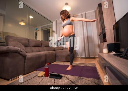 Giovane caucasica incinta donna stretching e facendo yoga in interni Foto Stock