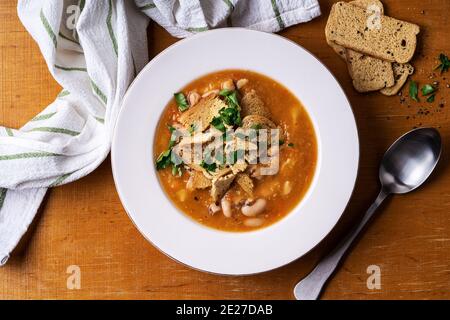 Ciotola di zuppa di lenticchie di pomodoro con fagioli e toast sottili e croccanti su fondo di legno. Pasto vegano, cibo a base di piante, vista dall'alto Foto Stock