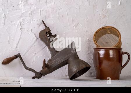 Una pentola di argilla, un filtro in legno e un dispositivo metallico per spremersi contro una parete bianca. Vecchi accessori per la casa. Sfondo chiaro. Foto Stock