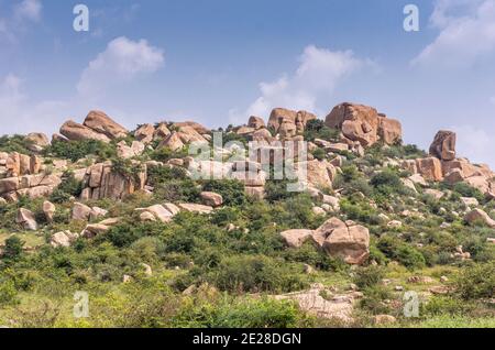 Hampi, Karnataka, India - 5 novembre 2013: KudureGombe mandapam e pozzo antico. Paesaggio intorno con massi marroni dispersi su verde cespuglio copertura Foto Stock