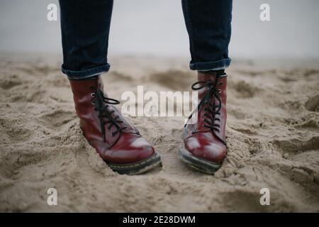 Scarponi da hipster rossi sporchi nelle sabbie con blu scuro jeans mare Foto Stock