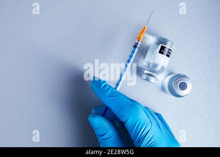 Una mano guanto contiene una siringa con flaconcini di vetro da vaccino liquido trasparente per la scienza in background Foto Stock