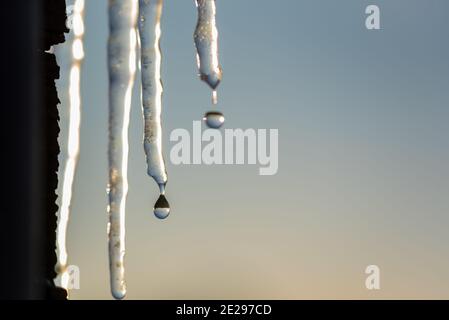 Fusione di iciclette nei raggi del sole che tramonta. Il riflesso dell'orizzonte in gocce d'acqua in caduta. Cambiamento di tempo e di temperatura in inverno. Foto Stock