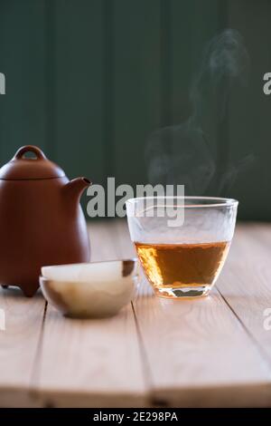 Concetto di bevanda sana. Tè cinese vecchio puerh bollente in chahai di vetro e una tazza di pietra onice su spazio copia tavolo di legno bianco. Stile minimalista Foto Stock