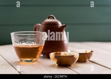 Concetto di bevanda sana. Tè cinese vecchio shen puerh in teapot di argilla, chahai di vetro e tazze onice su spazio di copia tavolo di legno bianco. Ancora vita con natu Foto Stock