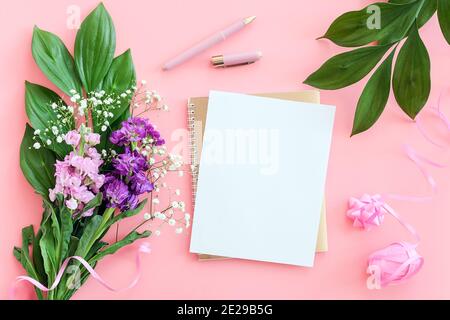 Foglio bianco vuoto su blocco note in oro a spirale con penna per il tuo testo o disegno e bouquet di fiori su sfondo rosa. Concetto Mockup area di lavoro femminile Foto Stock