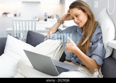 Donna caucasica durante una conversazione online. Si siede sul divano a casa e sta conversando tramite la comunicazione video. Foto Stock