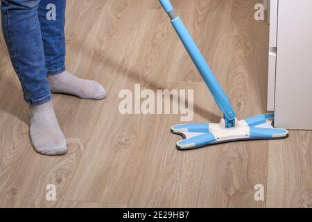 Un uomo lava i pavimenti con un mop in camera. Sotto il letto. Pulizia. Foto Stock