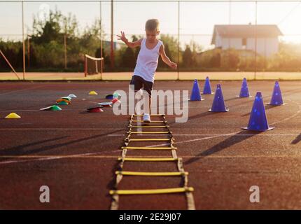 Piccolo ragazzo sulla mattina presto allenamento estivo saltando sopra tramacchi in campo di allenamento. Foto Stock