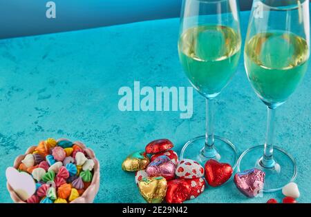 San Valentino o cena romantica con cuori di caramelle, bicchieri di champagne e un tavolo elegante su sfondo blu Foto Stock