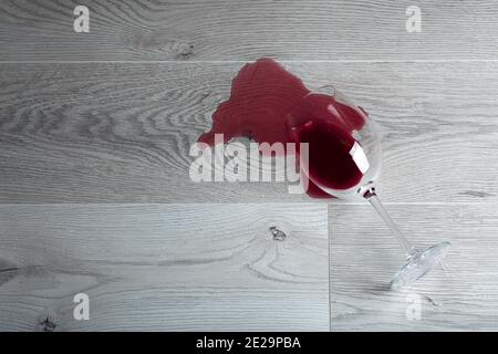 Pavimento in legno con bicchiere rovesciato di vino rosso. Vino versato su un pavimento in laminato di legno (parquet) con protezione dall'umidità. Foto Stock