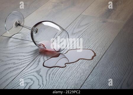 Pavimento in legno con bicchiere rovesciato di vino rosso. Vino versato su un pavimento in laminato di legno (parquet) con protezione dall'umidità. Foto Stock