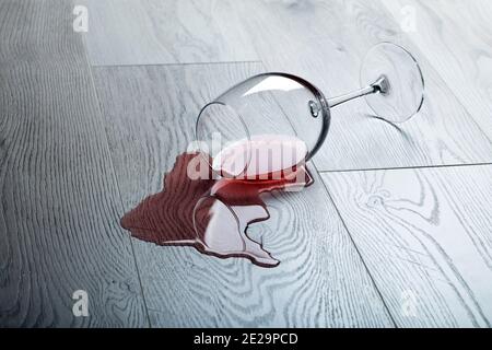 Pavimento in legno con bicchiere rovesciato di vino rosso. Vino versato su un pavimento in laminato di legno (parquet) con protezione dall'umidità. Foto Stock