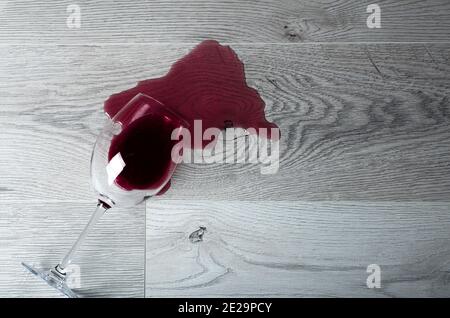 Pavimento in legno con bicchiere rovesciato di vino rosso. Vino versato su un pavimento in laminato di legno (parquet) con protezione dall'umidità. Foto Stock