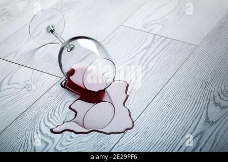 Pavimento in legno con bicchiere rovesciato di vino rosso. Vino versato su un pavimento in laminato di legno (parquet) con protezione dall'umidità. Foto Stock