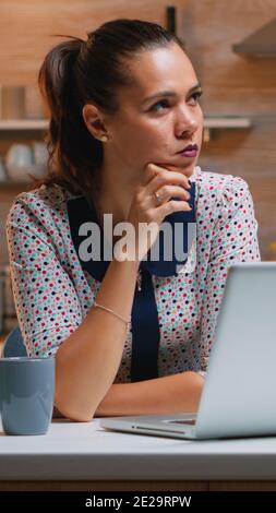 Pensando al prossimo progetto mentre si lavora a distanza da casa, leggere le attività utilizzando il computer portatile seduto in cucina. Dipendente impegnato e focalizzato che utilizza la moderna rete wireless che fa straordinari per scrivere lavori, cercare Foto Stock