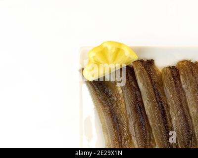 Sardine salate inscatolate con olio d'oliva su un piatto con un cuneo di limone Foto Stock