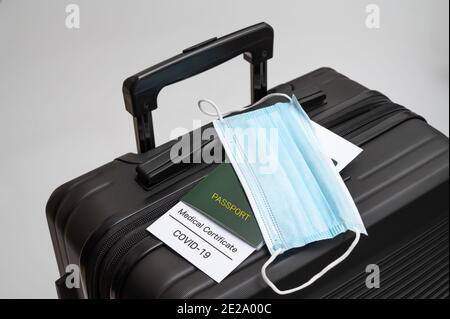 Un certificato sanitario COVID-19, passaporto e maschera medica su una valigia nera. Concetto di business post-COVID-19. Foto Stock
