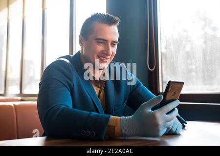 Ragazzo caucasico uomo d'affari in un vestito blu e guanti protettivi guarda nel telefono e sorride. Foto Stock