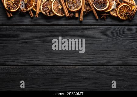 Sfondo di legno nero con arance secche, cannella e stelle di anice. Ripresa dall'alto. Sfondo e texture. Foto Stock