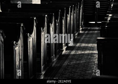 Mistero del tempio. Panchine di legno in chiesa vuota scura. La luce del sole illumina le torce e il pavimento di passaggio con motivo. Background religioso. Bianco nero Foto Stock